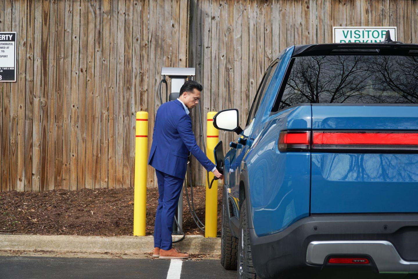 Man in a blue suit plugs a blue electric pickup truck into a Blink EV charging station